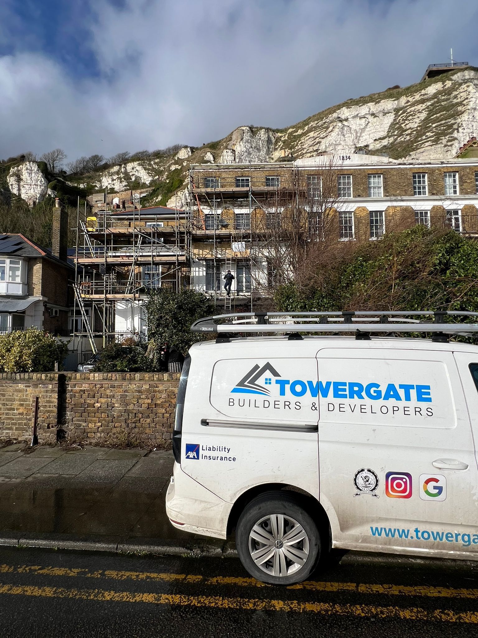 A towergate van is parked on the side of the road in front of a building under construction.