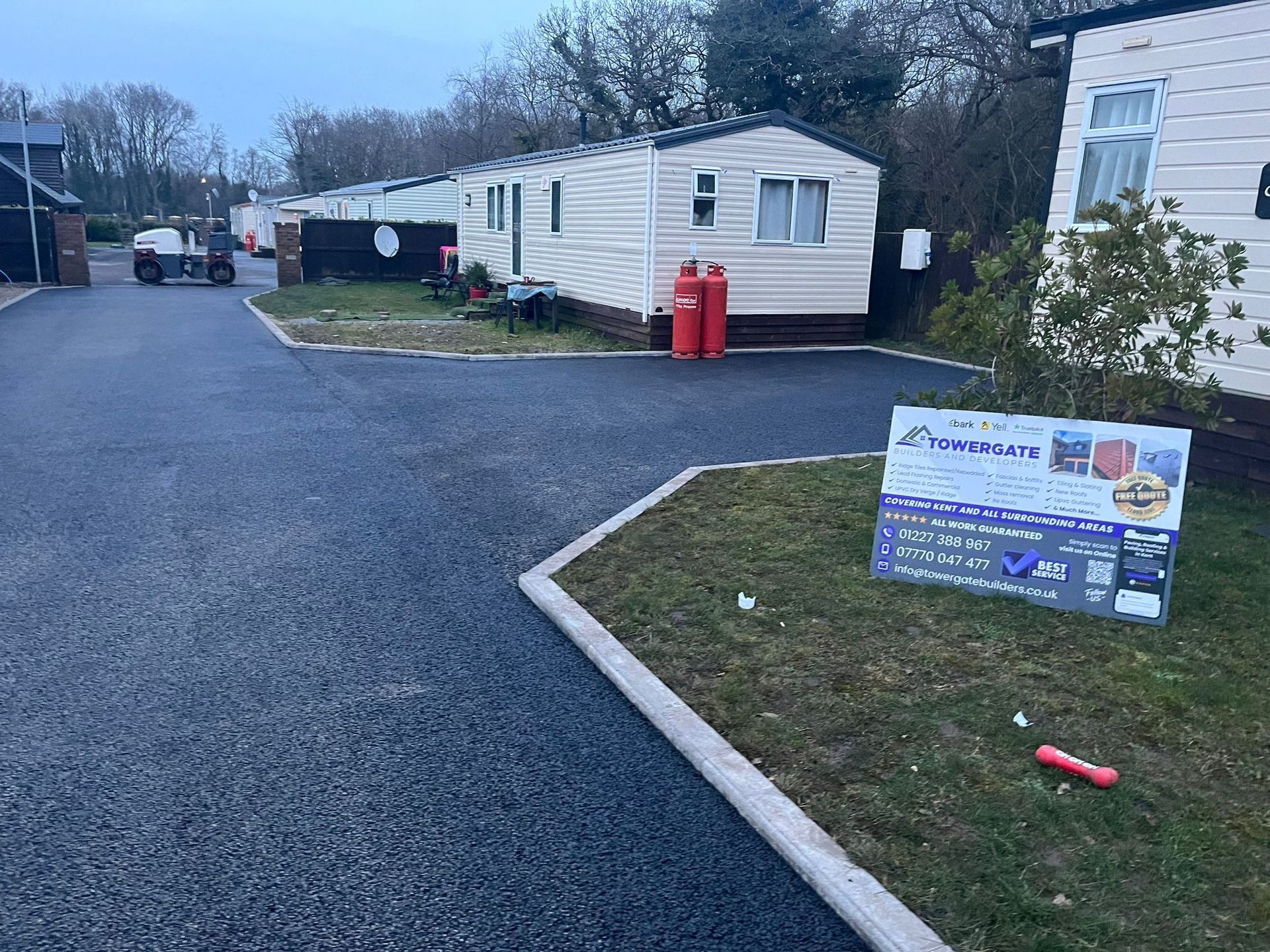 A sign is sitting in the grass in front of a row of mobile homes.