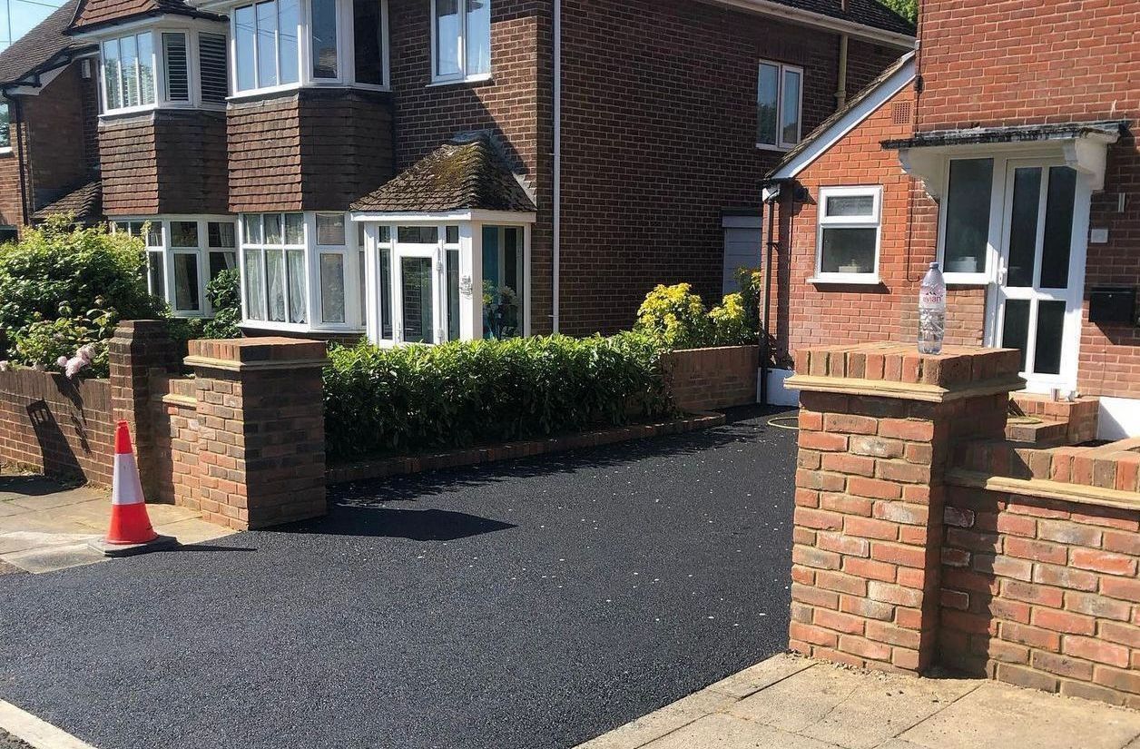 A brick house with a black driveway and a red cone in front of it.