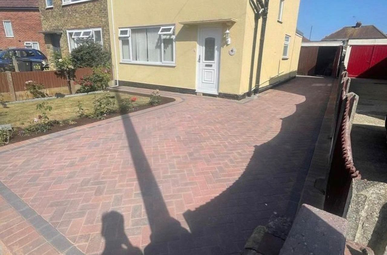 A person is standing in front of a house with a brick driveway.