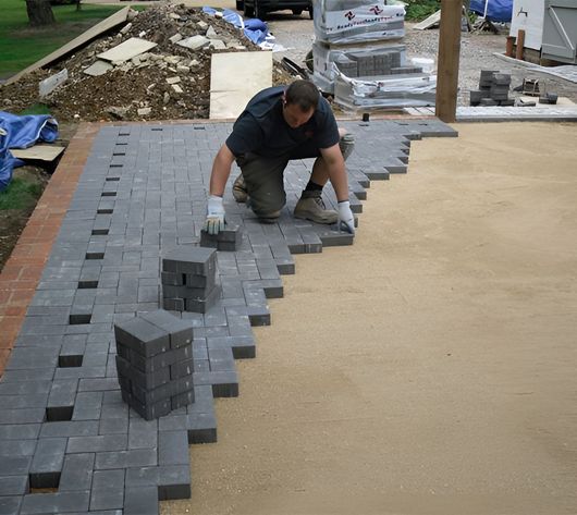 A man is laying bricks on a concrete surface