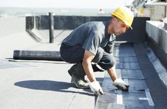 A man wearing a hard hat is working on a roof.