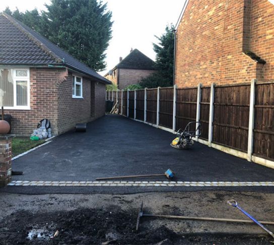 A driveway leading to a house with a wooden fence