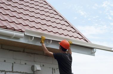 A man is installing a gutter on the side of a house.