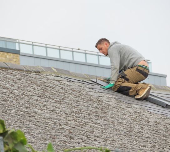 A man is kneeling on the roof of a building