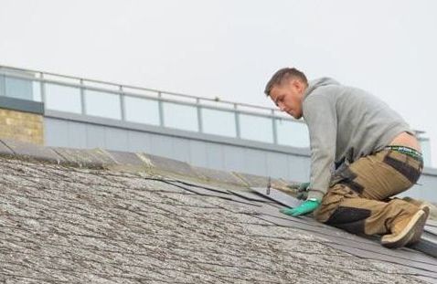 A man is kneeling on the roof of a building.