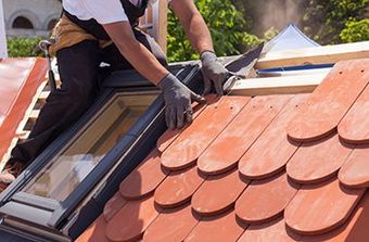 A man is sitting on top of a roof installing a skylight.