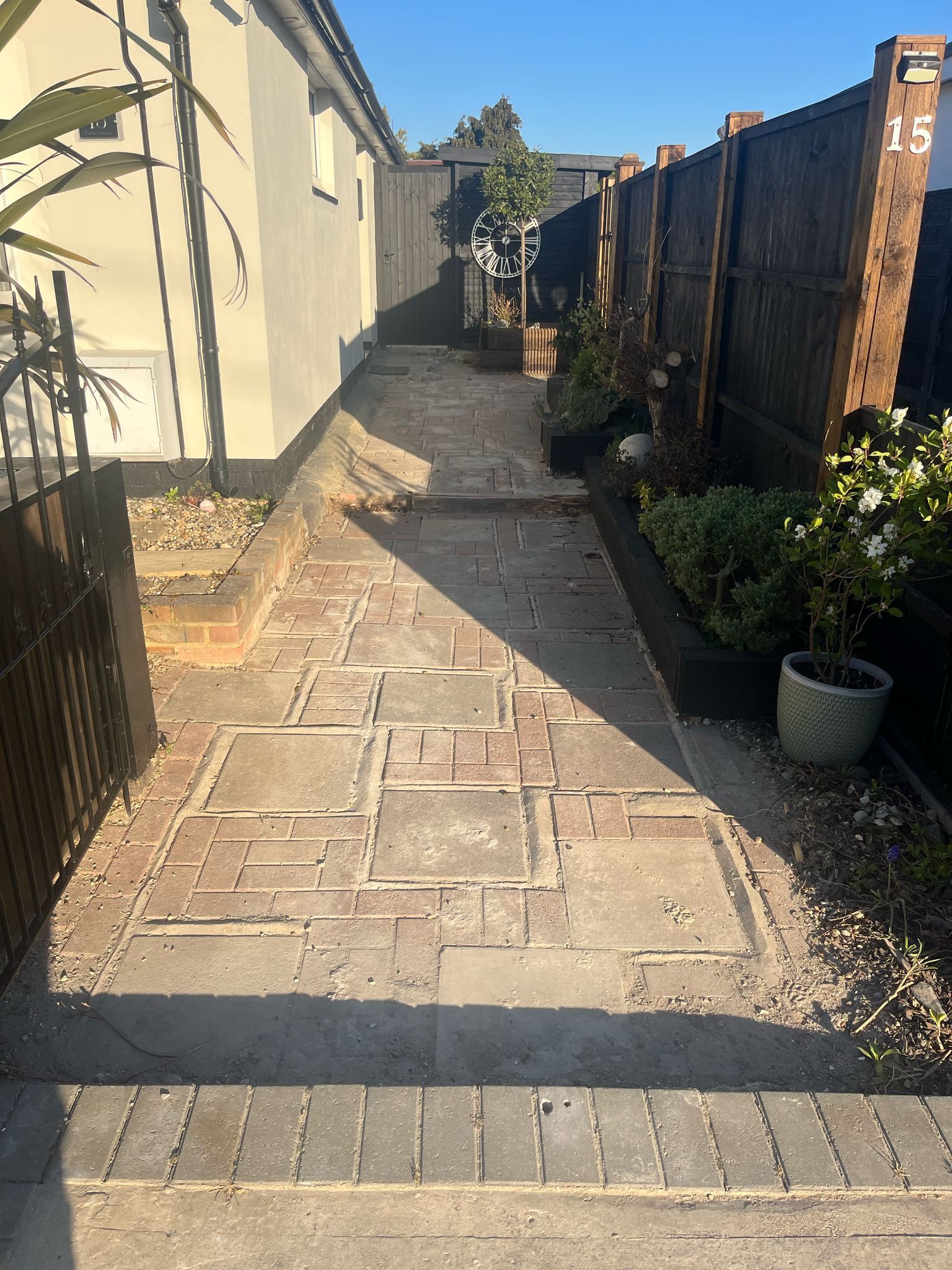 A brick walkway leading to a house with a wooden fence.