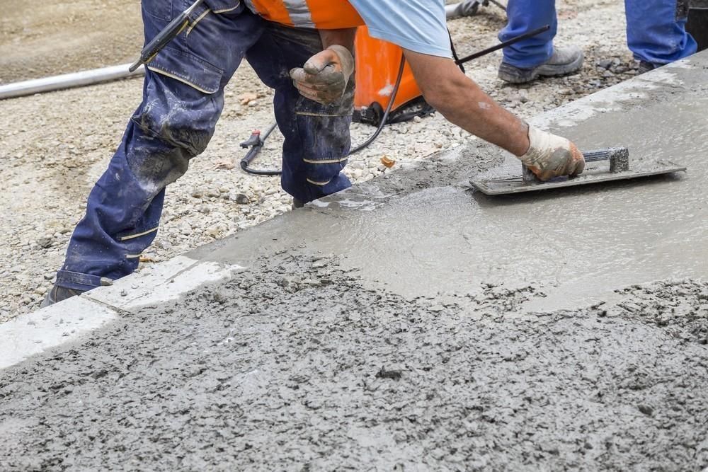 a construction worker is spreading concrete on the ground with a trowel .
