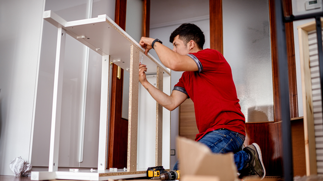 A man in a red shirt is kneeling down and working on a table.