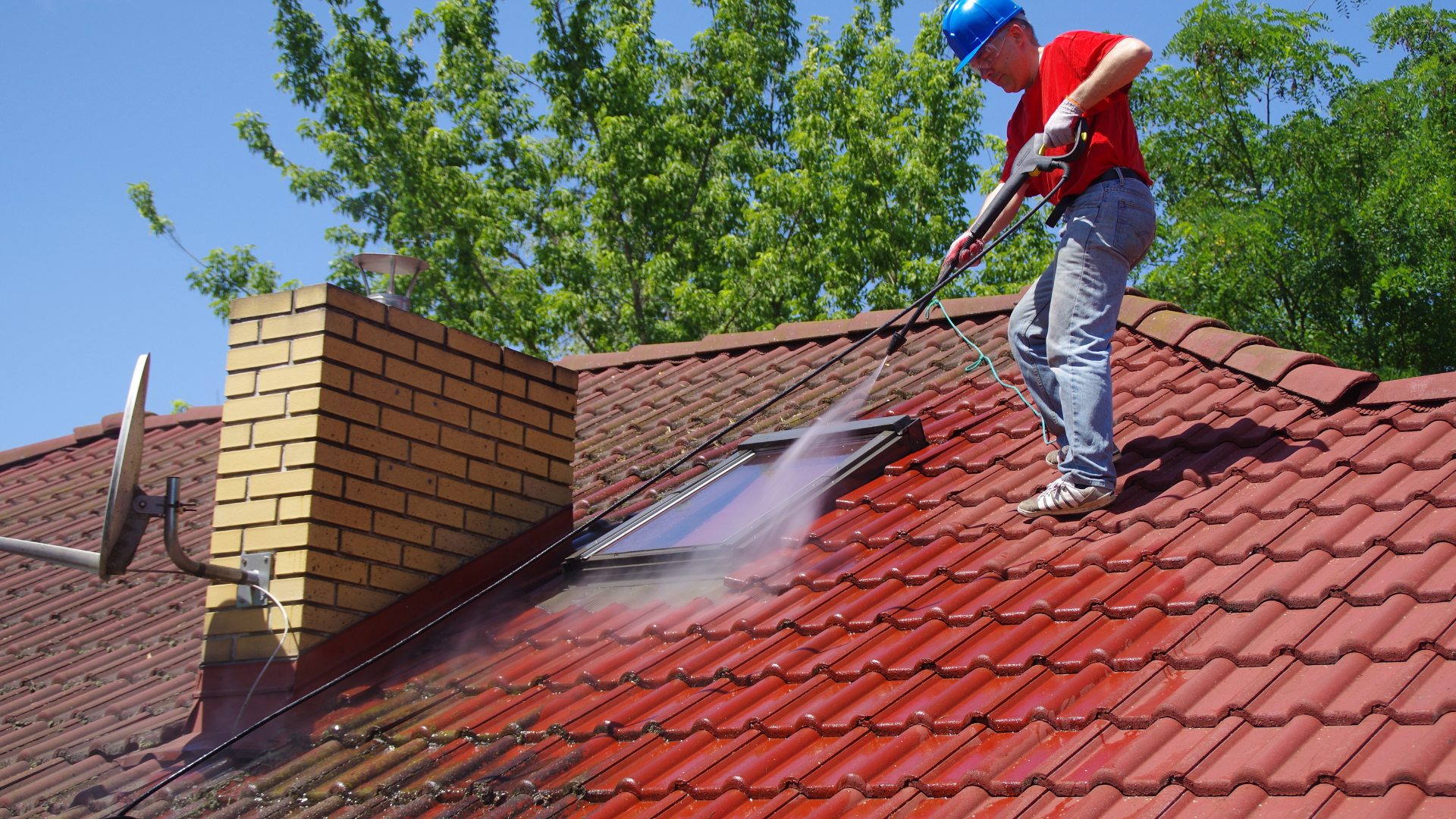 A man is cleaning a roof with a high pressure washer