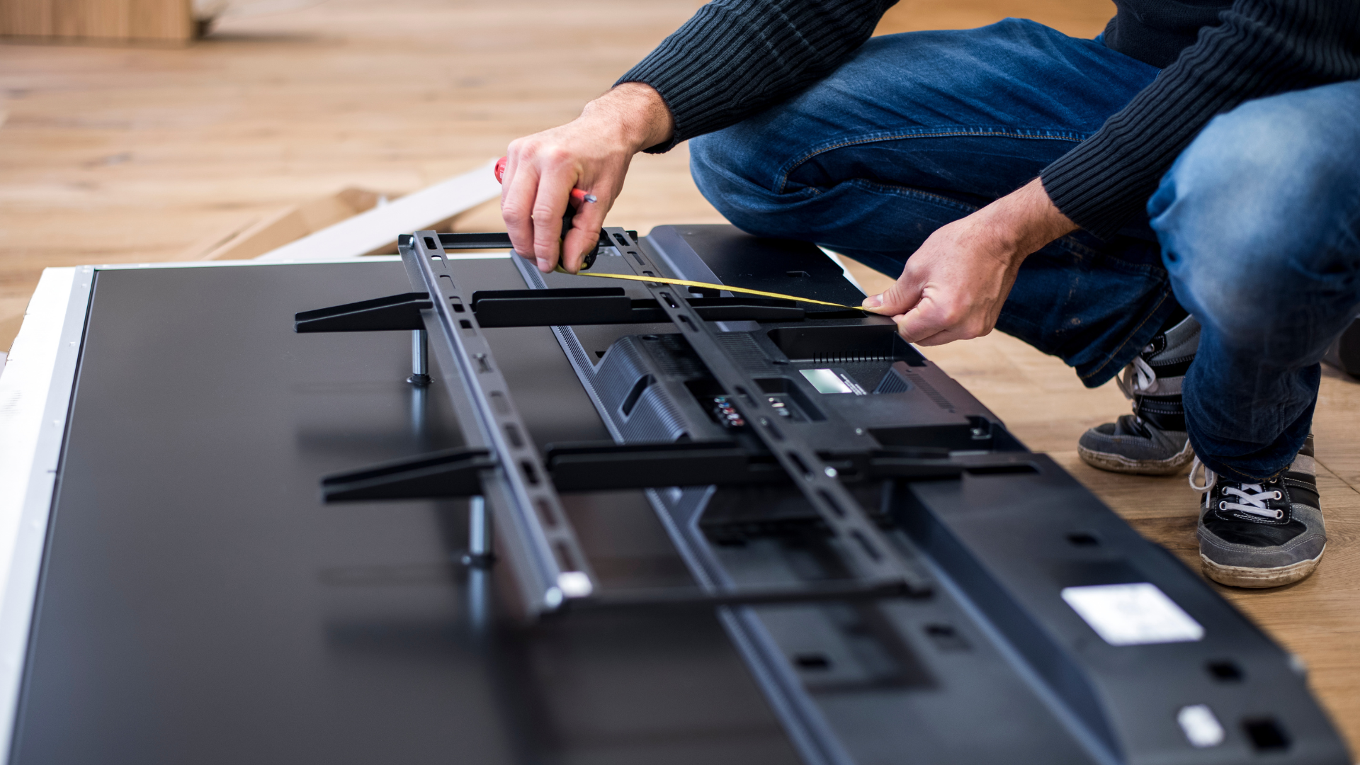 A man is kneeling down to install a flat screen tv.