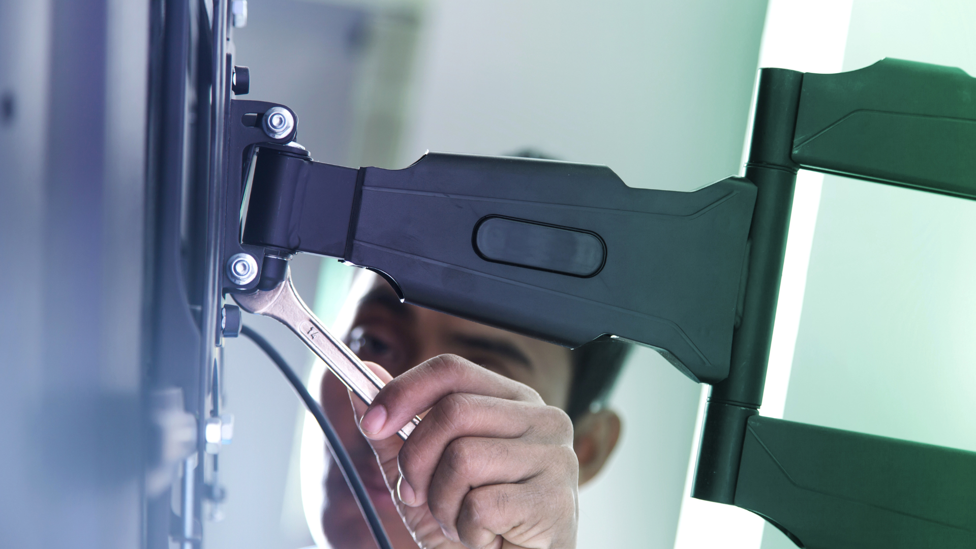 A man is fixing a tv mount with a wrench.