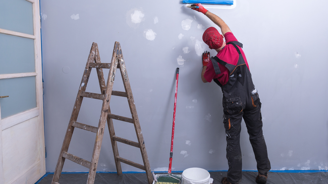 A man is painting a wall next to a ladder.