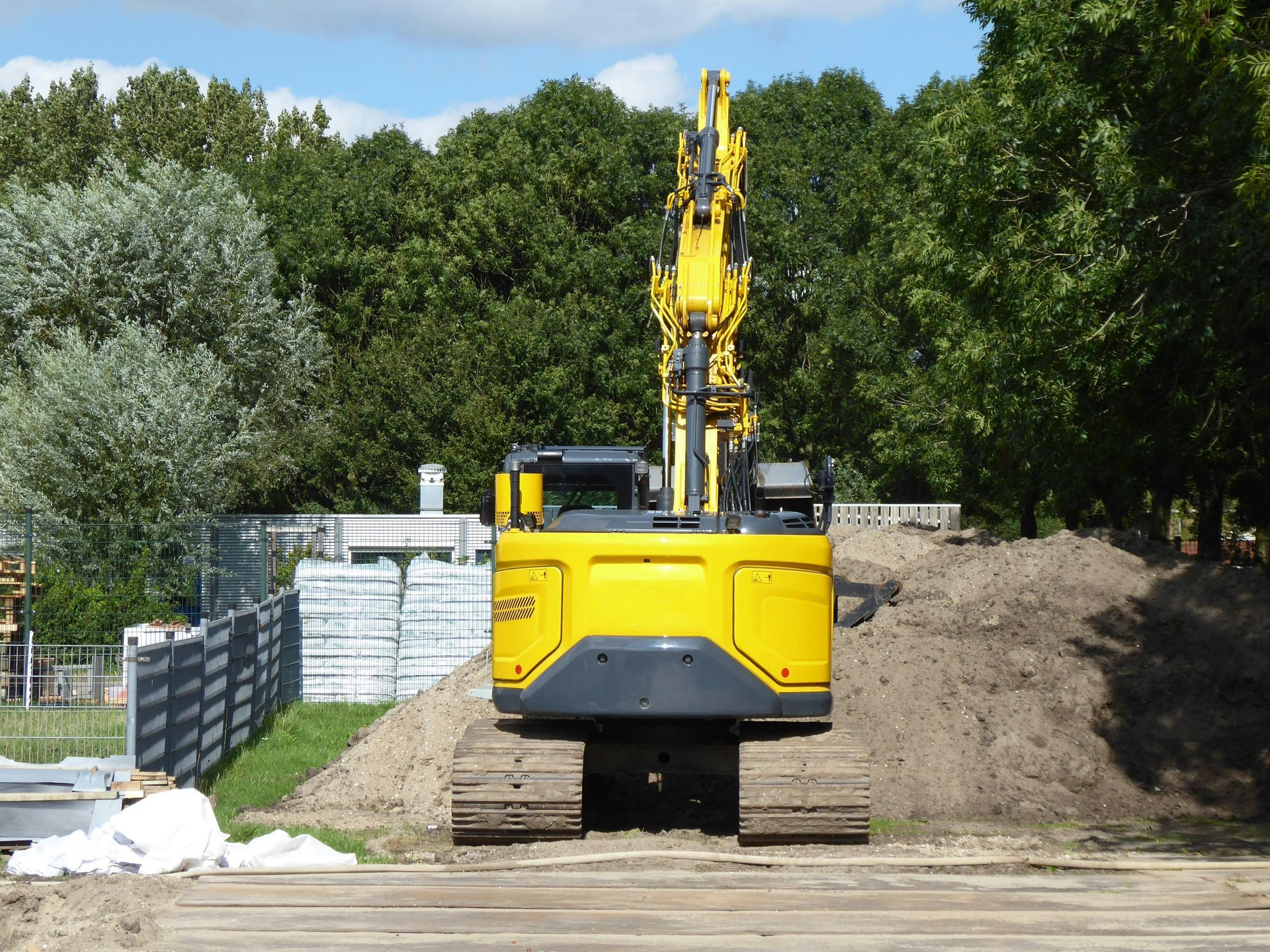 A yellow excavator parked in front of a dirt mound with trees in the background on a sunny day.
