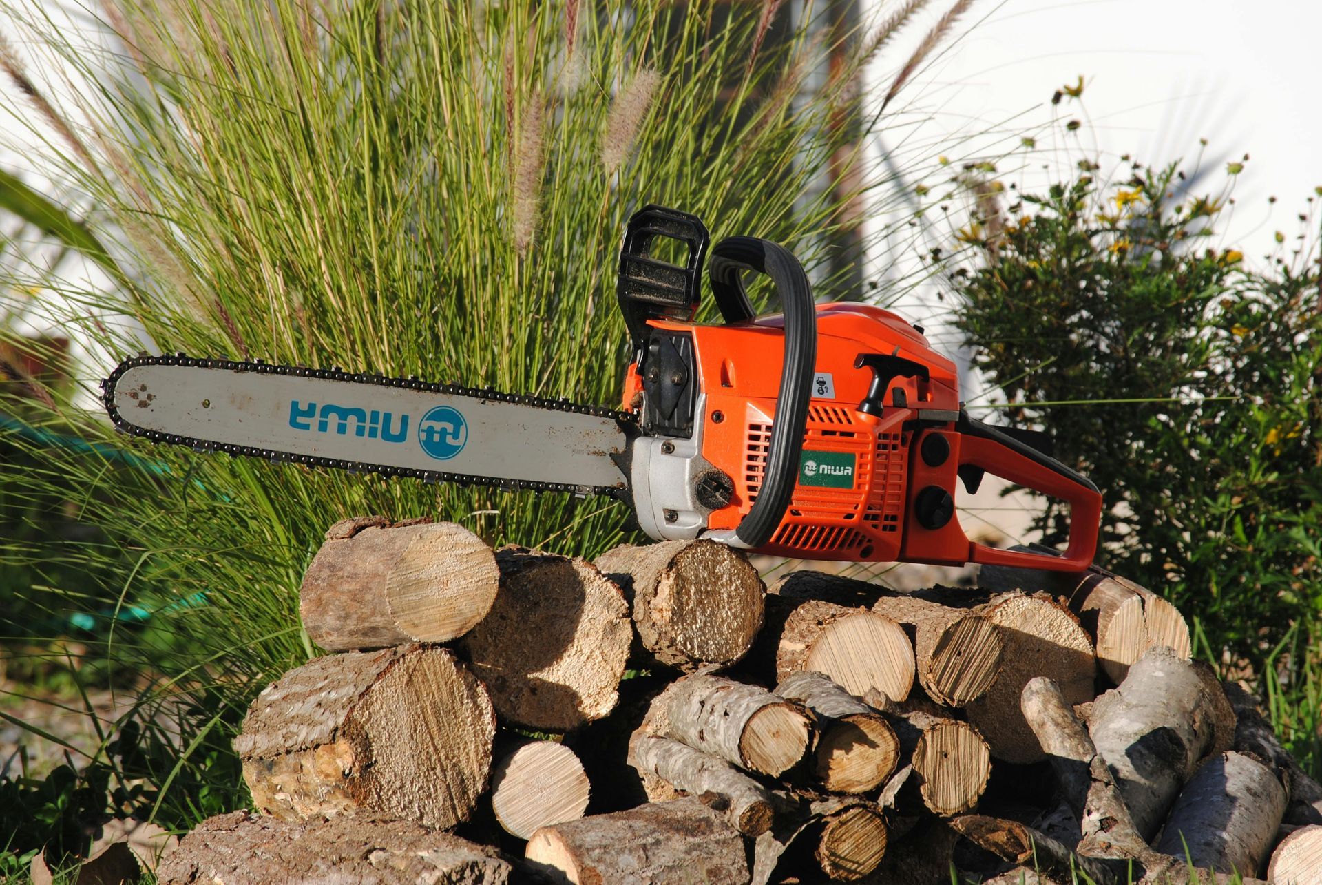 An orange chainsaw resting on a stack of cut wood in an outdoor garden setting.