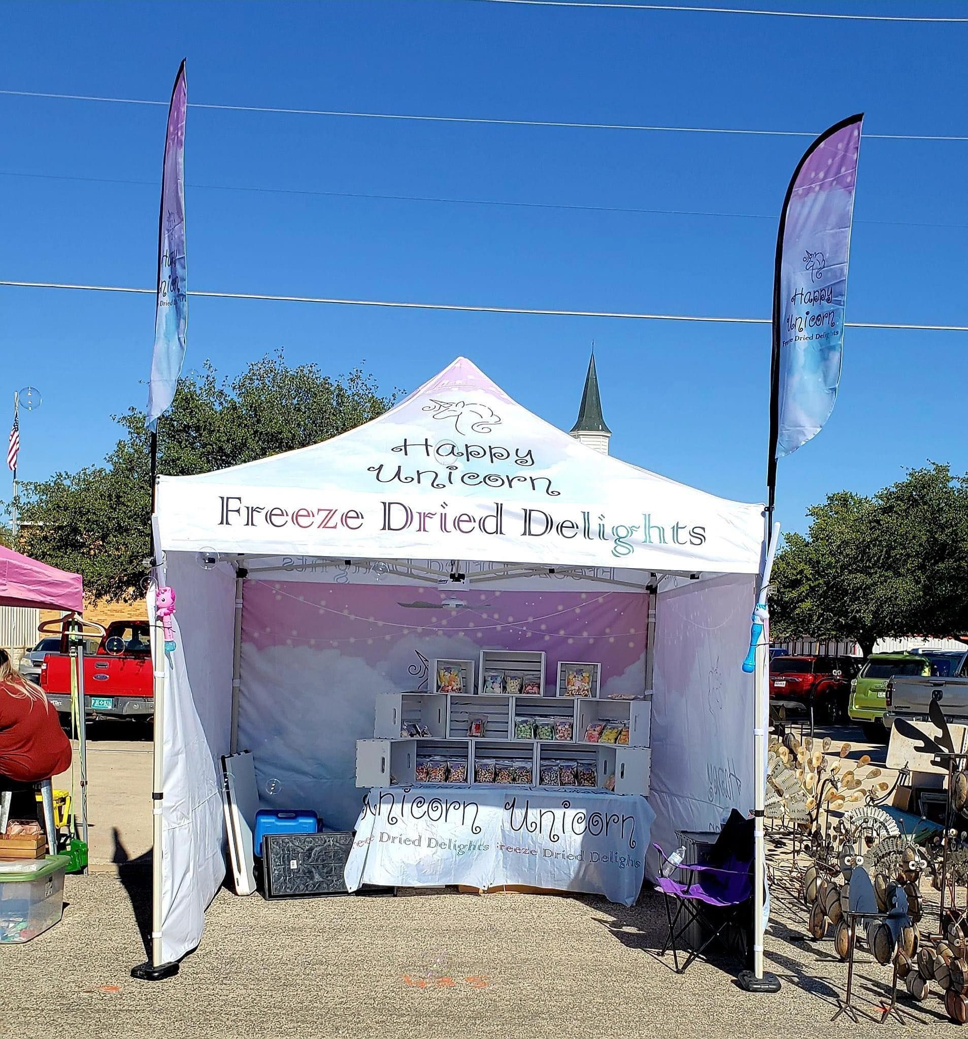 White vendor tent with shelves of packaged goods at an outdoor market on a sunny day