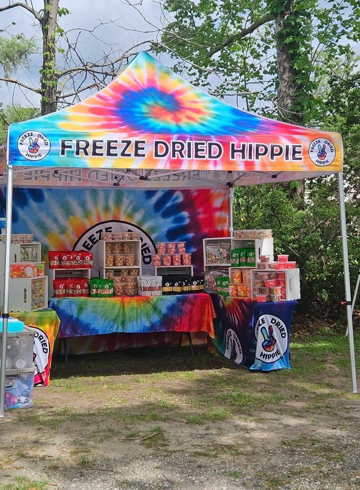 Tie-dye “FREEZE DRIED HIPPIE” booth with snacks and tables at an outdoor market