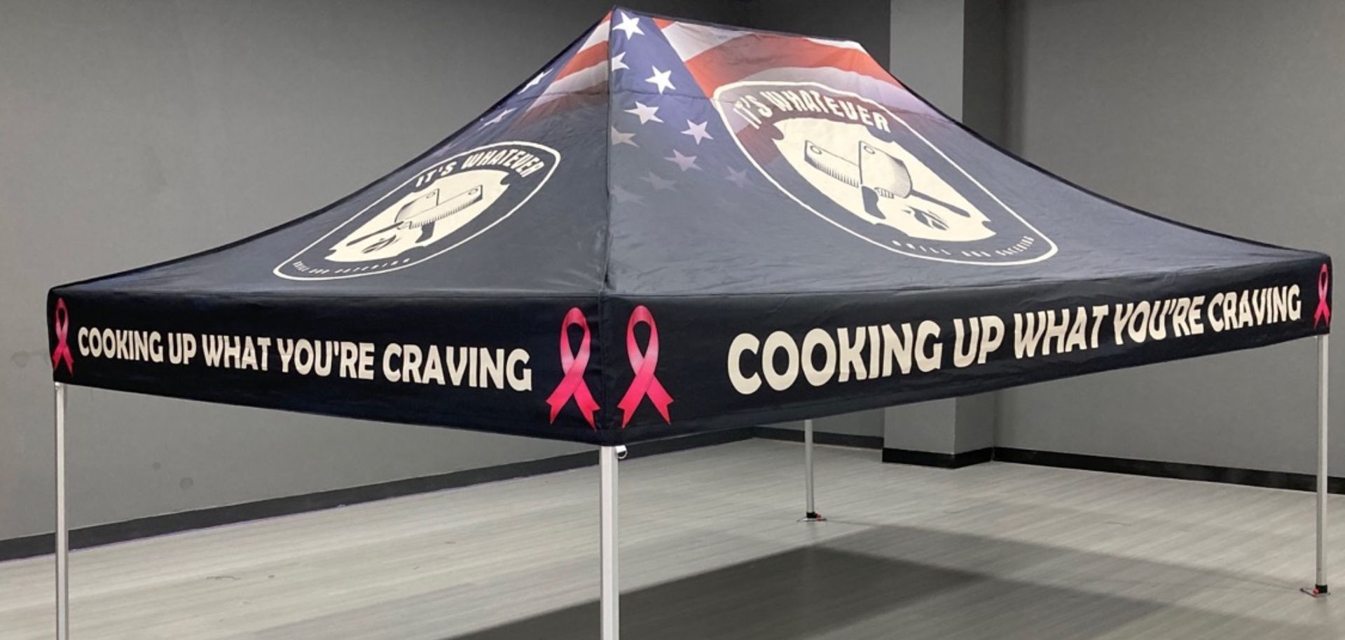 Black canopy tent with cancer awareness ribbons and slogan “Cooking up what you’re craving” on the valance.
