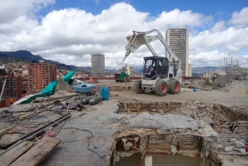Una excavadora está trabajando en una obra en construcción con una ciudad al fondo.