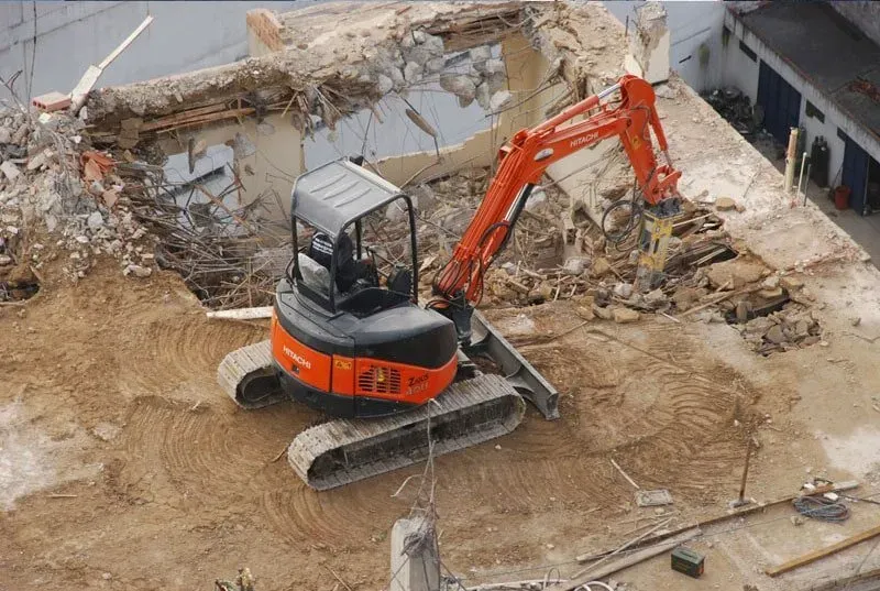 Se está utilizando una pequeña excavadora para demoler un edificio.