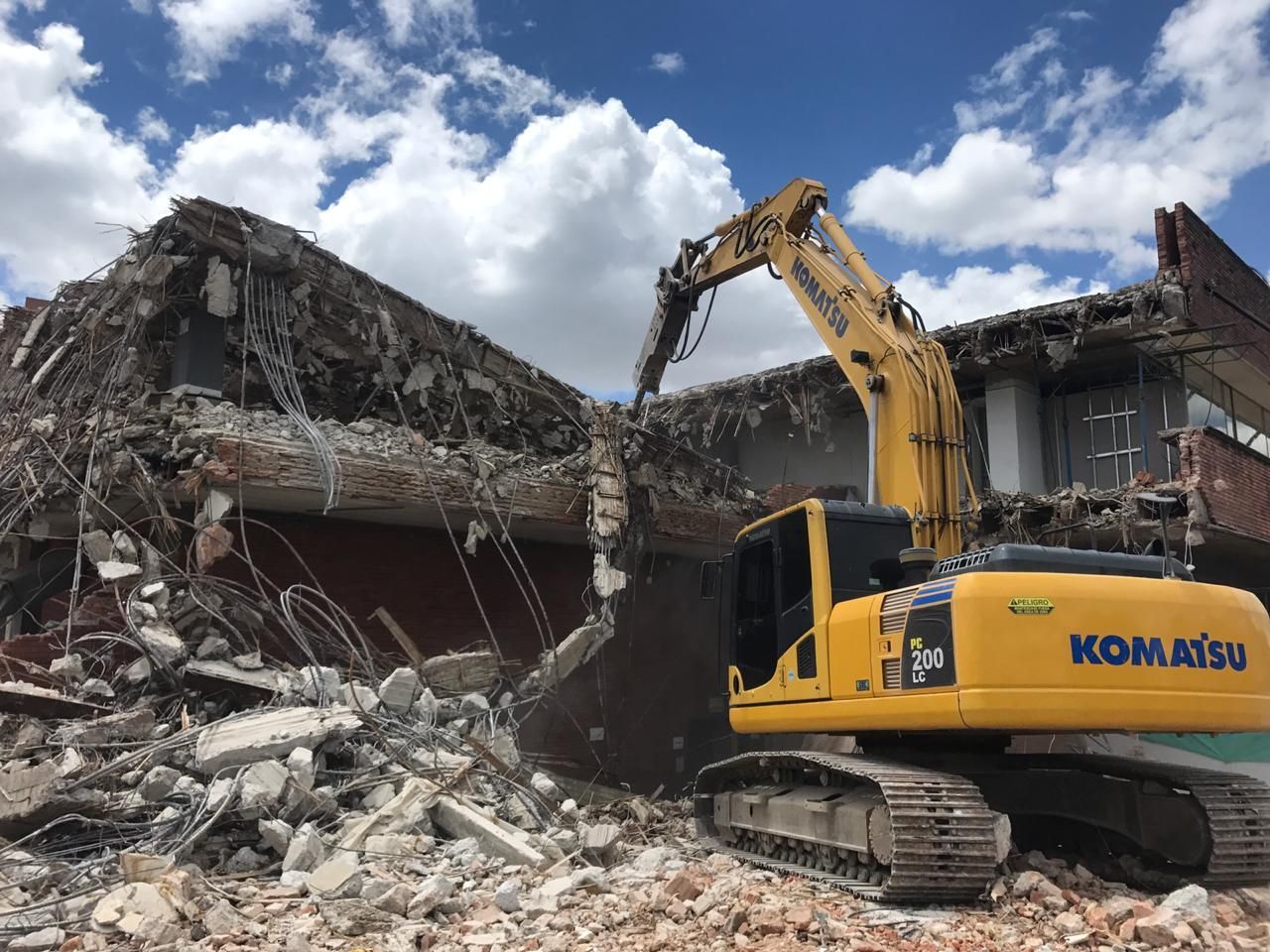 Una excavadora Komatsu amarilla está demoliendo un edificio.
