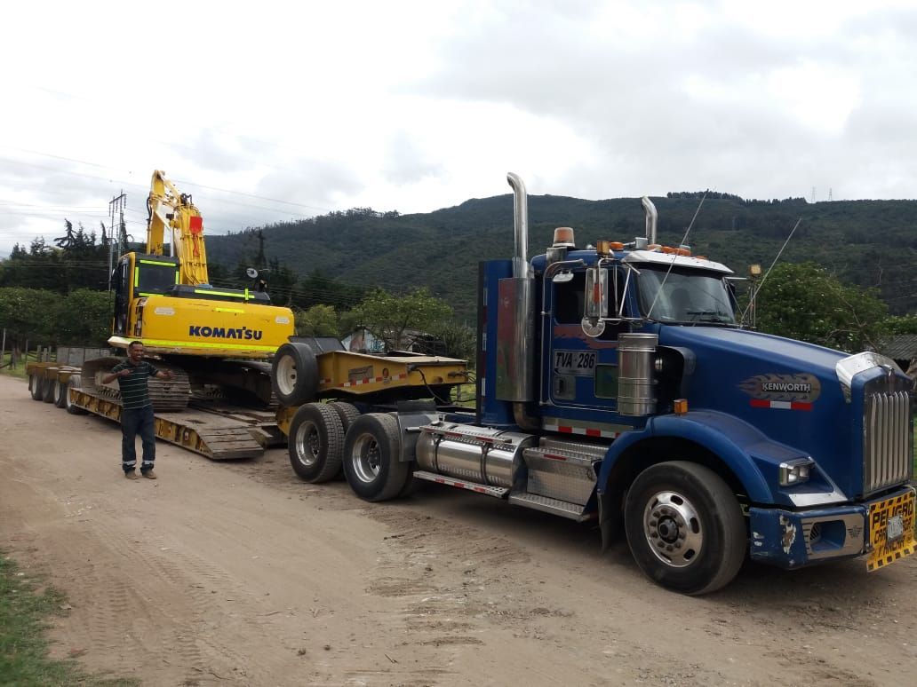 Un camión semirremolque azul transporta una excavadora amarilla en un remolque.