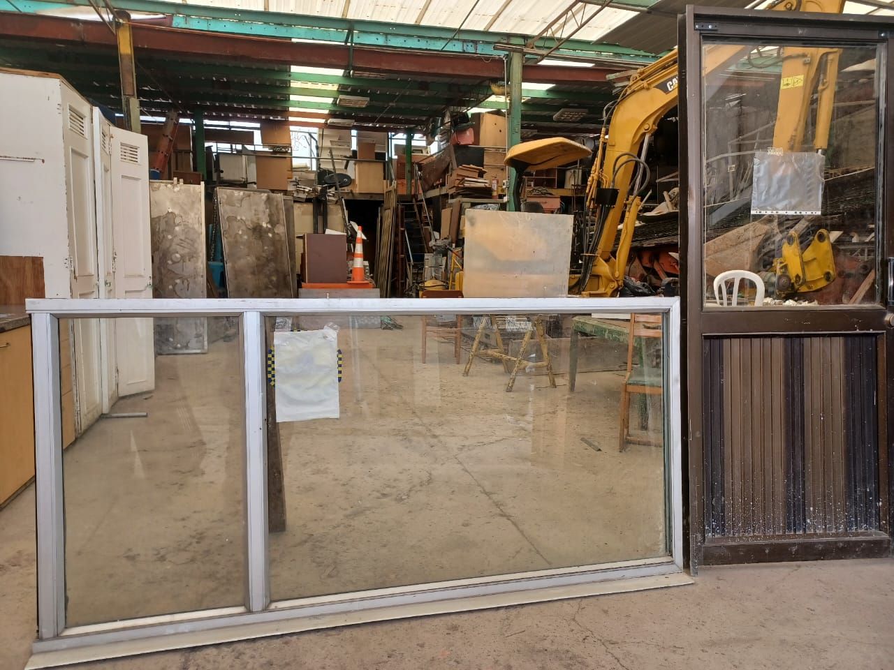 Una gran ventana en un almacén con una excavadora amarilla al fondo.