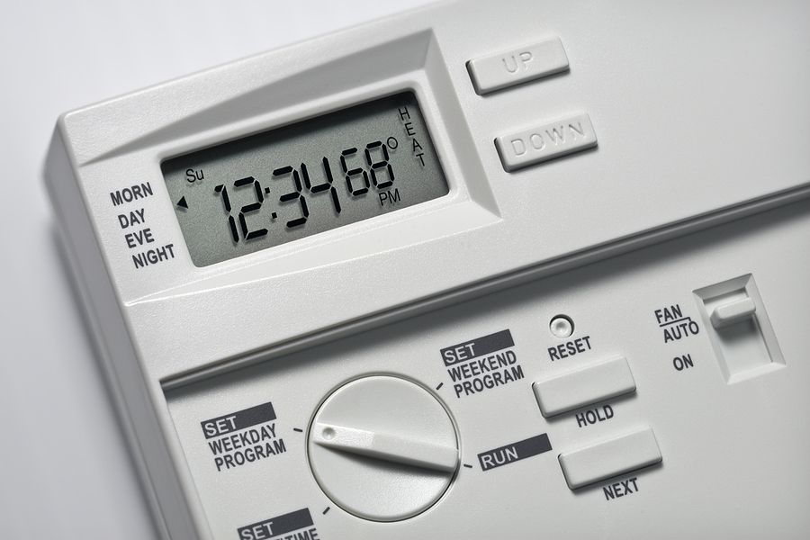 White thermostat with digital display showing time and temperature; buttons and dial visible.