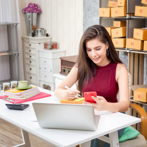 A woman is sitting at a desk with a laptop and a cell phone