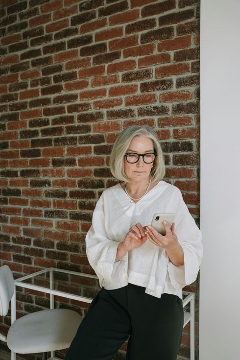 A woman is standing in front of a brick wall holding a cell phone.