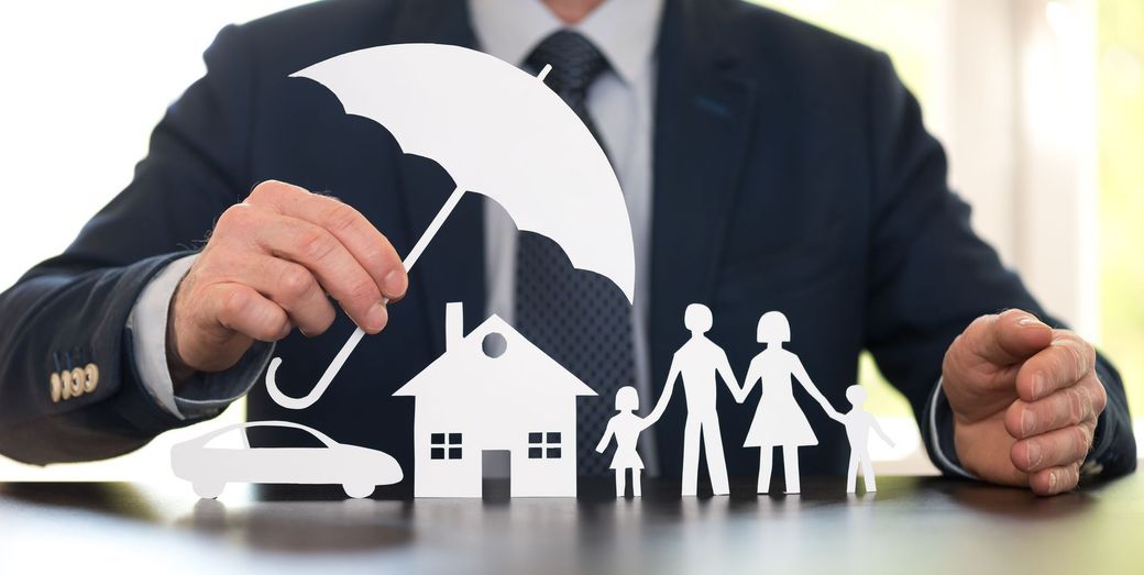 Un uomo tiene un ombrello sopra un ritaglio di carta raffigurante una casa, un'auto e una famiglia.