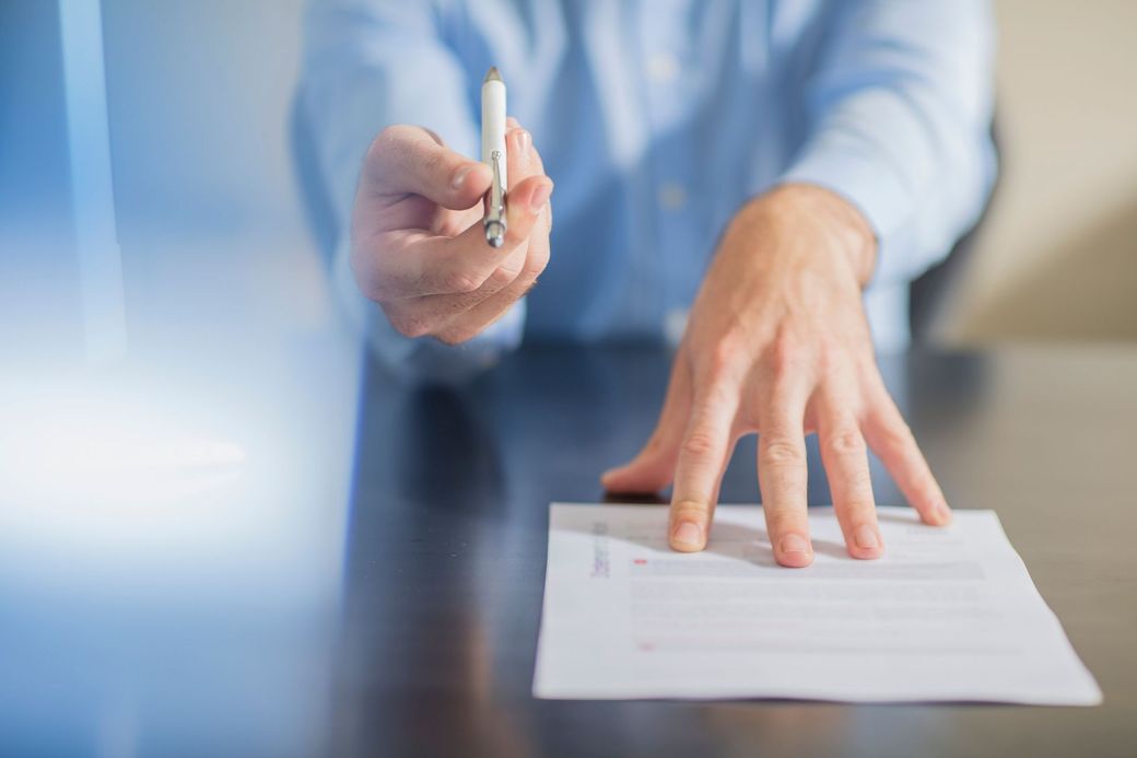 Un uomo è seduto a un tavolo e firma un documento con una penna.