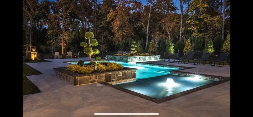A large swimming pool is lit up at night in a backyard surrounded by trees.