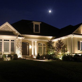 A large house is lit up at night with a full moon in the background.