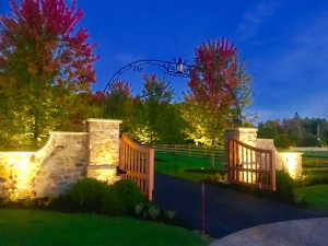 A wooden gate is surrounded by trees and a stone wall.