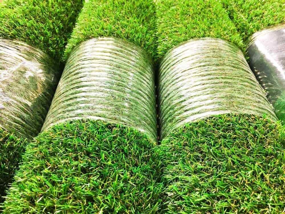 Close-up of rolled artificial turf with vibrant green blades and plastic backing, ready for installa