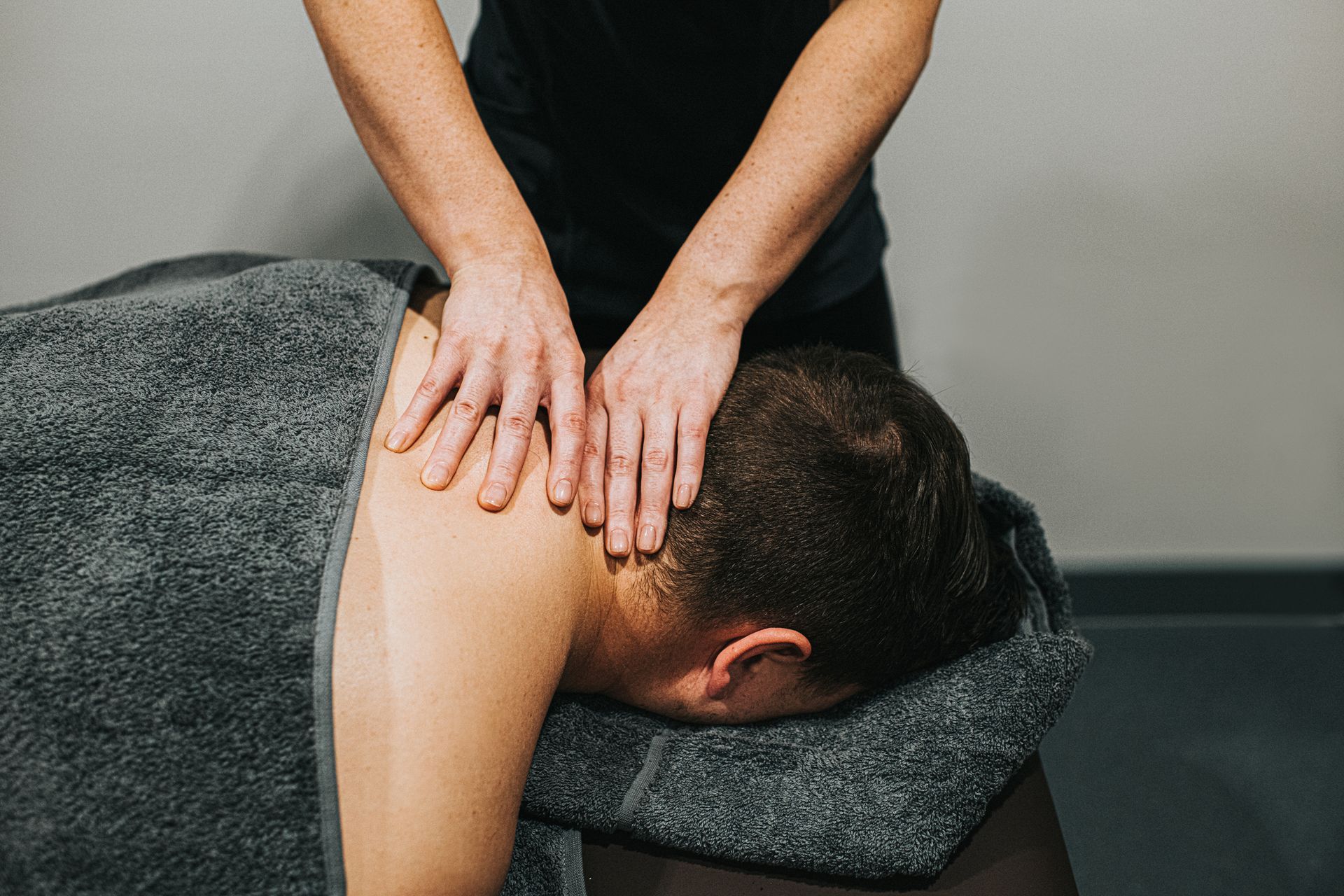 Person receiving a neck massage with hands pressing on the back of the neck in a room.