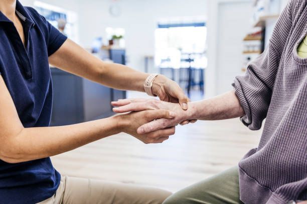 Therapist examining patient's wrist. Clinic interior; blue shirt, gray sweater.