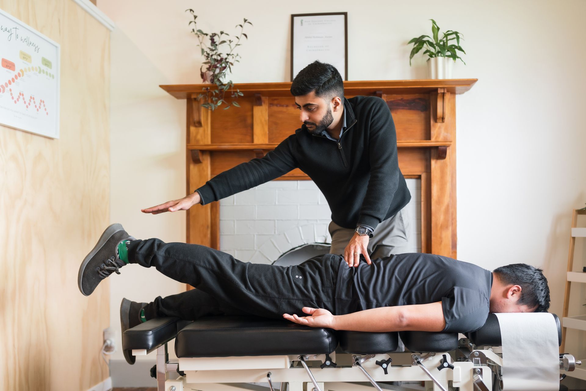 Chiropractor examining a patient on a treatment table. Brown fireplace in background.