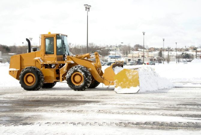 Yellow front loader pushing snow in a snowy parking lot