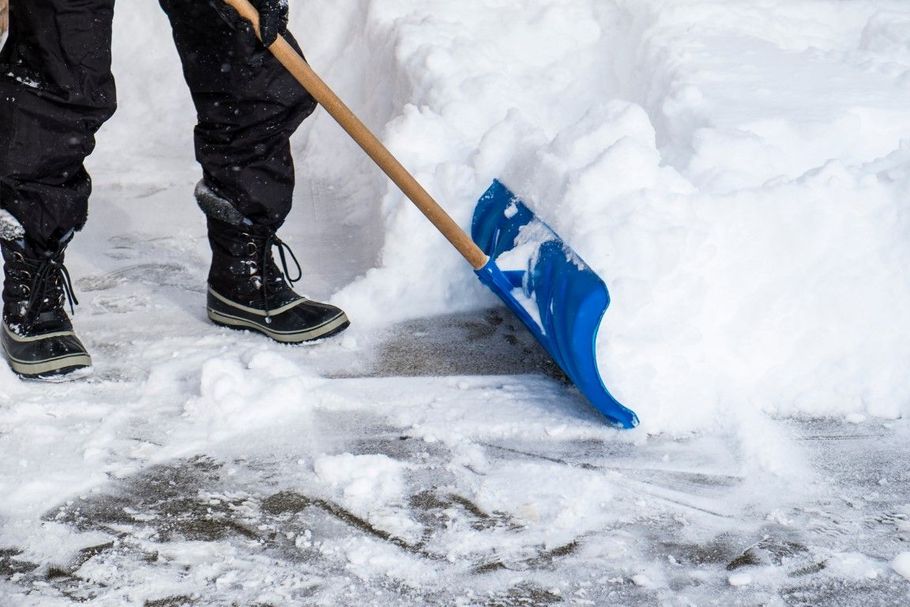 Person shoveling snow with a blue shovel on a snowy sidewalk