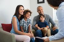 Family smiling while consulting with a person holding paperwork. Indoors, natural light.