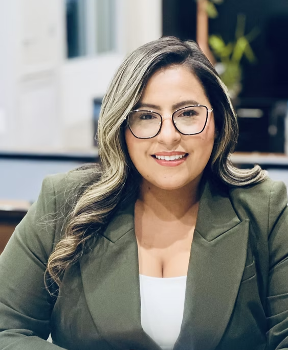Woman wearing glasses and green blazer smiles at the camera.