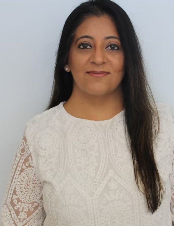 Woman with long, dark hair, wearing a white lace top, smiling slightly against a plain white background.