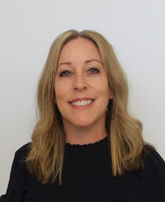 Woman with blonde hair smiles, wearing black shirt against a white backdrop.