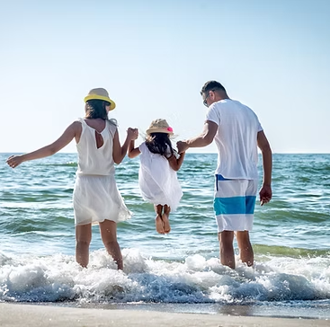Family wading into the ocean, holding hands. Sunlit beach scene, happy.