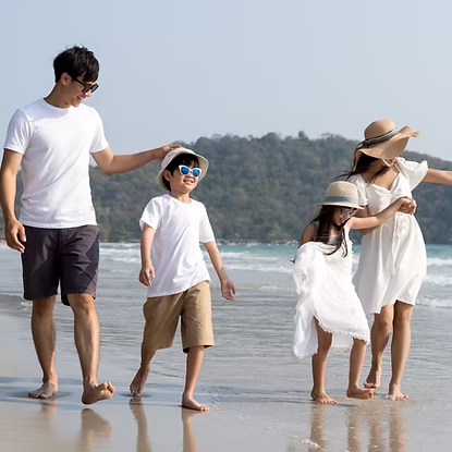 Family of four walking on a beach: father with sunglasses, two children, and mother in a dress.
