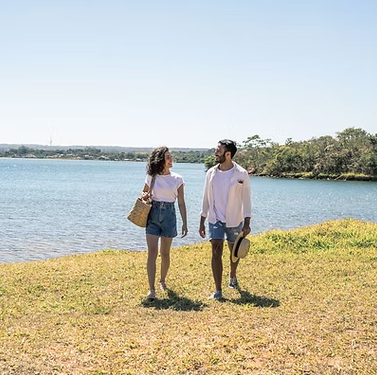 Couple walking on grassy shore, looking at each other, near a lake. Sunny day.