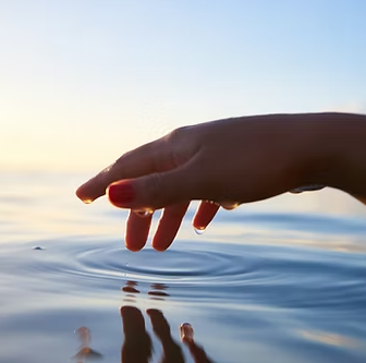 Hand with red nail polish touching water, creating ripples. Sky in background.